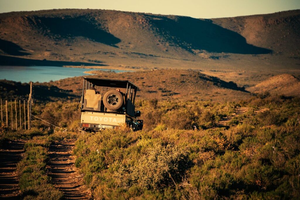 A rugged off-road vehicle traverses a mountain landscape near a serene lake at sunset.